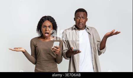 Wütende schwarze Frau, die ihr Smartphone vor grauem Hintergrund im Studio hält Stockfoto