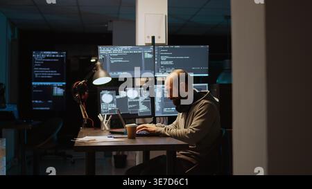 Softwareentwickler, der Quellcode auf einem Laptop und mehreren Monitoren eingibt und die Programmiersprache verwendet, um einen Firewall-Sicherheitsserver zu erstellen. Männlicher Programmierer, der Datenbank-Cloud-Computing entwickelt. Stockfoto