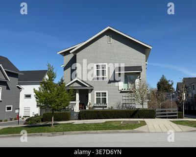 Modernes zweistöckiges Vorstadtfamilienhaus mit grauem Abstellgleis und weißer Verkleidung in Surrey, British Columbia, Kanada. Schuss an einem klaren Tag im 9. April 2026. Stockfoto
