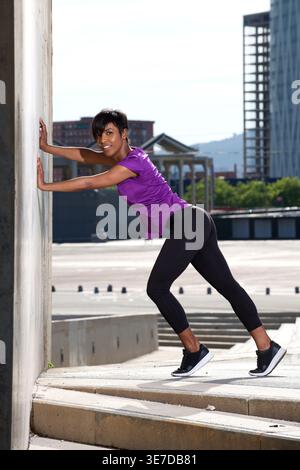 Lächelnde schwarze Frau, die an sonnigen Tagen im Freien Stretching-Workout macht Stockfoto