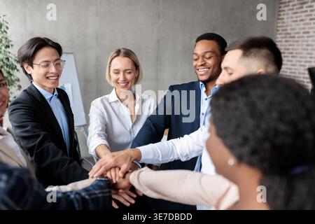 Verschiedene Gruppen von Geschäftsmitarbeitern stapeln sich die Hände zusammen, während sie im Büro im Kreis stehen Stockfoto