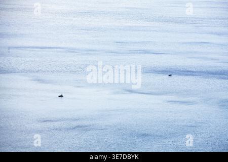 Blick aus einem hohen Winkel auf einen riesigen ruhigen See oder Meeresoberfläche mit zwei kleinen Silhouetten von Booten, die ein Gefühl von Skala und Ruhe schaffen. Stockfoto