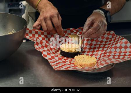 Close-up Chef-Hände, die Krabbenkuchen mit der runden Ringform in der Restaurantküche zubereiten. Szene der Lebensmittelzubereitung, die Formtechnik und Zutat hervorhebt Stockfoto