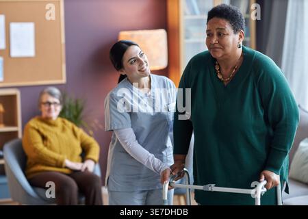 Gemischte Krankenschwester hilft älteren schwarzen Frauen mit kurzen Haaren mit Mobilitätsläufern im Altersheim Stockfoto