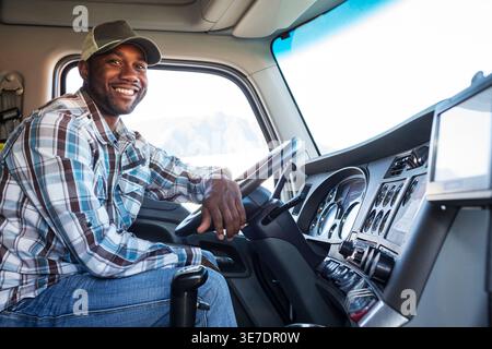 Lächeln Schwarzer männlicher Lkw-Fahrer, der sich auf das Lenkrad lehnt und im Lkw sitzt Stockfoto