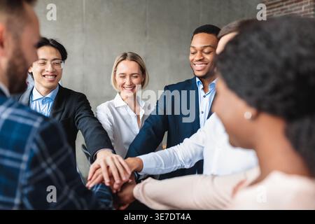 Verschiedene Gruppen von Geschäftsmitarbeitern stapeln sich die Hände zusammen, während sie im Büro im Kreis stehen Stockfoto