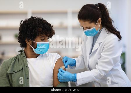 Asiatische Ärztin in Operationshandschuhen, die Klebeband an der Schulter eines asiatischen männlichen Patienten auf Stuhl in der Klinik anbringen Stockfoto