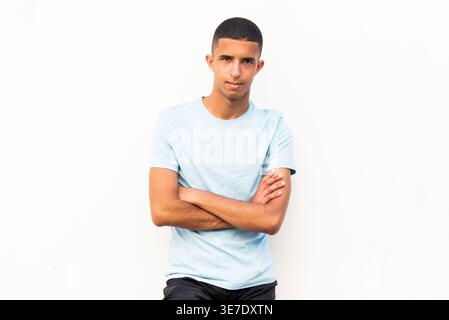 Arabischer Mann mit gekreuzten Armen, der tagsüber an die weiße Wand gelehnt ist Stockfoto