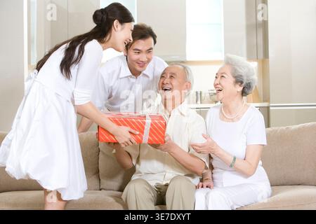 Überraschter chinesischer Mann, der von seiner Familie zu Hause ein Geschenk erhält Stockfoto