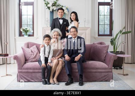 Chinesisches Seniorenpaar mit Enkel, der auf der Couch sitzt, während ein Paar daheim hinter ihnen steht Stockfoto