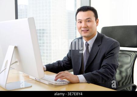 Lächelnder chinesischer Geschäftsmann, der am Tisch im Büro sitzt Stockfoto