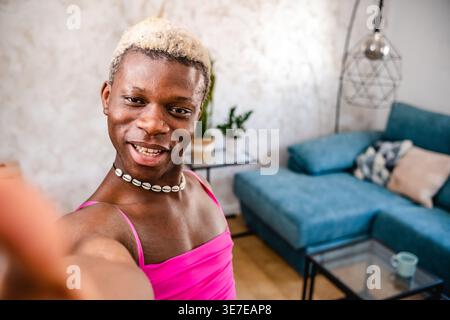 Lächelnde schwarze nicht-binäre Person, die zu Hause im Wohnzimmer Selfie macht Stockfoto
