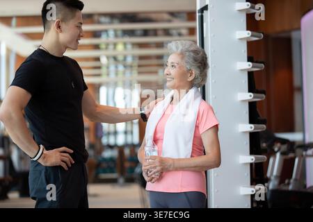 Lächelnde Chinesin, die mit männlichem Personal Trainer steht und nach dem Training im Fitnessstudio eine Pause einlegt Stockfoto