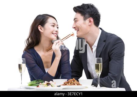 Lächelnde Chinesin, die ihren Freund mit Essstäbchen am Tisch im Restaurant füttert Stockfoto