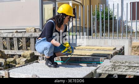 Hispanische Arbeiterin mit Denim-Overall und gelbem Helm, die tagsüber auf der Baustelle auf grauen Sandsteinen sitzt Stockfoto