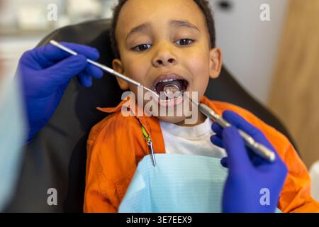 Schwarzer Junge bei Zahnbehandlung mit männlichem Zahnarzt in der Klinik Stockfoto