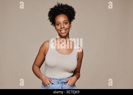 Porträt einer jungen afroamerikanischen Frau, die vor neutralem Hintergrund und natürlicher Schönheit lächelt und dabei die Kamera anschaut Stockfoto