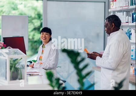 Japanische Apothekenassistentin, die tagsüber in der Nähe eines älteren schwarzen männlichen Mitarbeiters in der Apotheke steht Stockfoto