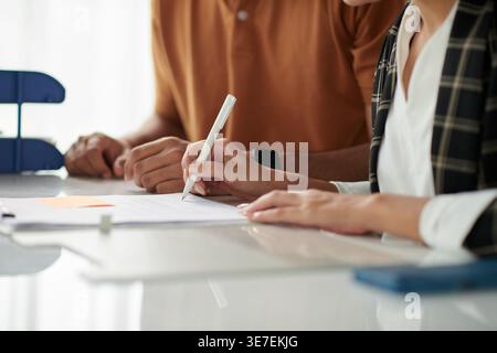 Asiatische und gemischte Rassenpaare unterzeichnen Dokumente, die zusammen am Tisch im Büro sitzen Stockfoto