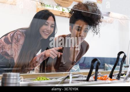 Zwei Freundinnen suchen Essen im Restaurant und diskutieren, entscheiden, was sie bestellen sollen Stockfoto