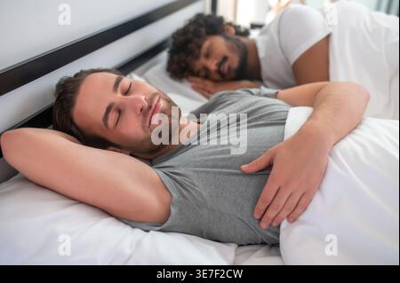 Indische und kaukasische Schwule schlafen zusammen im Bett zu Hause Stockfoto
