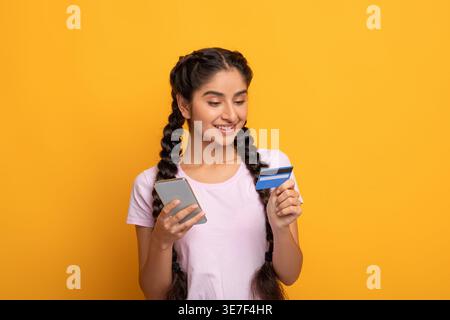 Indische Frau mit Smartphone und Kreditkarte, die vor gelbem Hintergrund steht Stockfoto
