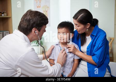 Mutter gemischter Rasse, die den Sohn umarmt und einen männlichen kaukasier ansieht, der seinen Atem in der Klinik hört Stockfoto