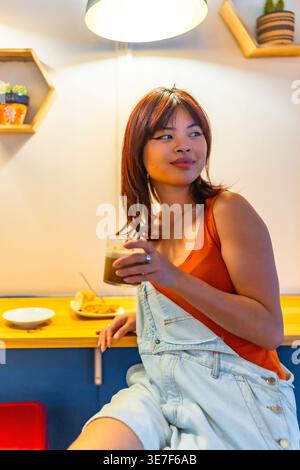 Asiatische Frau, die ein Glas Kaffee hält und im Café wegschaut Stockfoto
