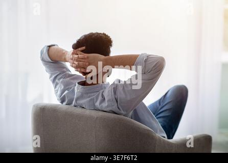 Arabischer Mann mit Bart und Händen hinter dem Kopf, der auf einem Sessel sitzt Stockfoto