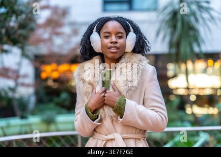 Schwarze Frau mit Afro, die Ohrenschützer und Wintermantel im Park trägt Stockfoto