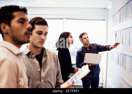 Schwarze Frau im Business-Anzug analysiert chLifestyles an der Wand mit einem kaukasischen Kollegen im Büro Stockfoto