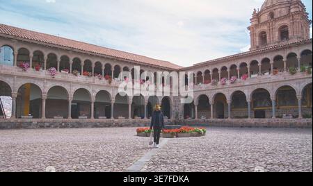Hispanische Touristenfrau mit Hut und Jacke vor dem Tempel der Sonne der Inkas in Cusco, Peru Stockfoto