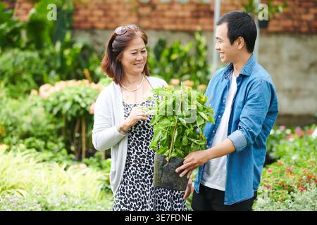 Asiatischer männlicher Arbeiter hilft asiatischen Kunden mittleren Alters, Pflanzen auf dem Pflanzenmarkt zu finden Stockfoto