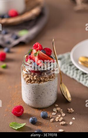 Ein mehrschichtiges Frühstücksparfait besteht aus cremigem Chia-Pudding mit knusprigem Müsli und frischen Erdbeeren. Die rustikale Umgebung umfasst einen goldenen Löffel Stockfoto