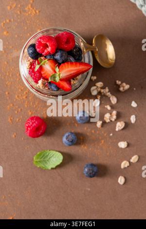 Ein Blick von oben auf ein lebhaftes Frühstücksparfait mit frischen Beeren und Müsli. Die Szene bietet warmes natürliches Licht auf einem strukturierten braunen Sur Stockfoto