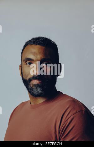 Bärtiger Mann in braunem Hemd, der im Studio an der weißen Wand steht Stockfoto