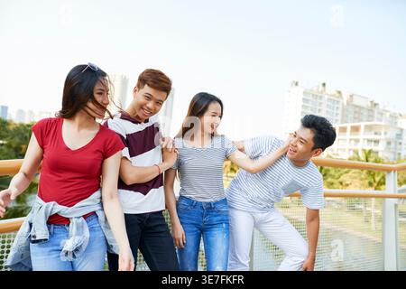 Lächelnde Gruppe asiatischer Freunde, die sich miteinander unterhalten, während sie auf der Überführung der Stadt stehen Stockfoto
