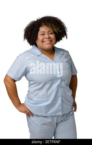 Große hispanische Frau mit lockigem Afro in blauer Uniform, die im Studio mit Händen in Taschen vor weißem Hintergrund steht Stockfoto