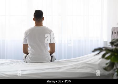Ein arabischer Mann, der wegschaut, während er zu Hause auf dem Bett sitzt Stockfoto