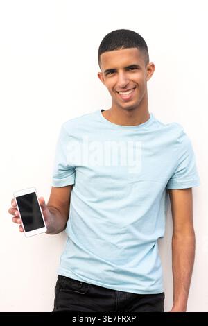 Lächelnder arabischer männlicher Teenager, der ein Smartphone vor weißem Hintergrund hält Stockfoto