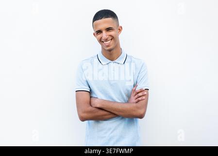 Lächelnder arabischer männlicher Teenager, der mit gekreuzten Armen vor weißem Hintergrund steht Stockfoto