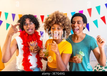 Verschiedene Freunde halten Cocktailgläser, die zu Hause zusammen tanzen Stockfoto