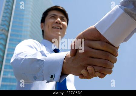 Ein chinesischer Geschäftsmann schüttelt die Hand mit einem Kollegen, der in der Nähe des Gebäudes in der Stadt steht Stockfoto