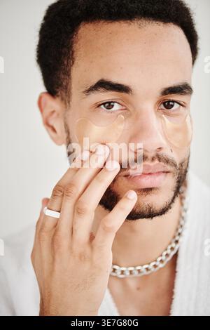 Ernsthafte gemischte Rasse bärtiger Mann, der Augenflecken aufträgt, die vor weißem Hintergrund im Studio stehen Stockfoto