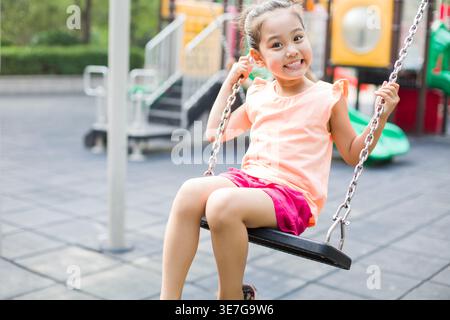 Lächelndes chinesisches Mädchen, das auf dem Spielplatz auf einer Schaukel sitzt Stockfoto