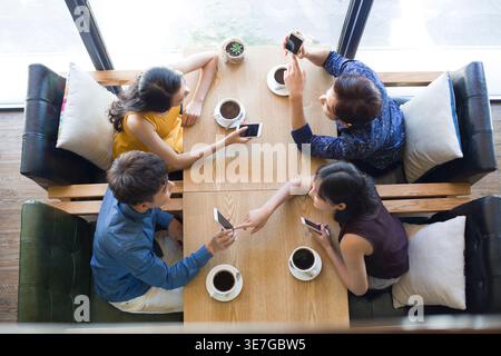 Chinesische Freunde, die Smartphones benutzen, während sie am Tisch im Café Kaffee trinken Stockfoto