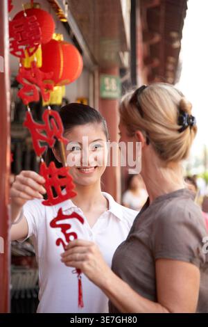 Chinesische Verkäuferin, die Produkte für kaukasische Touristen anbietet, die auf dem Markt stehen Stockfoto