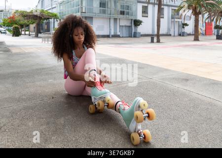 Hispanische Frau, die Rollschuhe bindet, während sie auf dem Boden in der Stadt sitzt Stockfoto