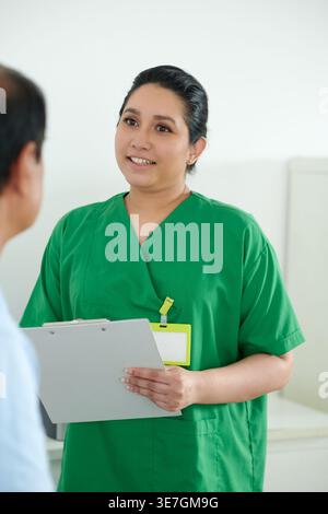 Asiatische Krankenschwester, die medizinische Zwischenablage hält, während sie spricht asiatischer männlicher Patient in der Klinik steht Stockfoto