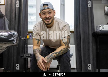 Lächelnder asiatischer Tätowierer, der tagsüber in seinem Tätowierstudio sitzt Stockfoto